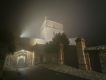 The tower and gate of a medieval castle in a small town during a winter night with fog, Castello di Seravalle, Emilia Romagna, Italy, Europe