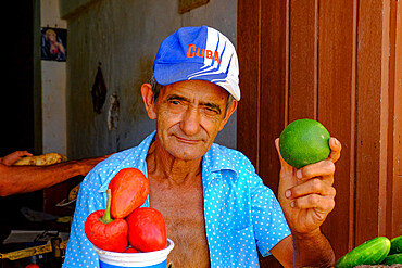 A man at a vegetable stand holds up a lime, Trinidad, Cuba, West Indies, Central America