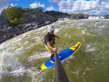 Skip Brown surfs his stand up paddleboard in fast moving whitewater on the Potomac River near Great Falls, Virginia, United States of America, North America