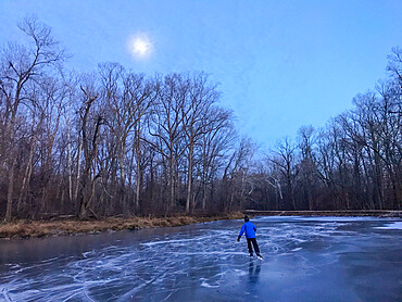 Man skates the frozen C and O Canal (Chesapeake and Ohio Canal) under a hazy full moon, Potomac, Maryland, United States of America, North America