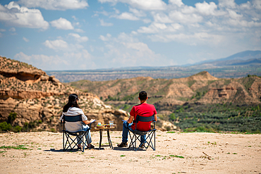 Couple sit on chairs with a table looking at a desert like landscape near Francisco Abellan Dam, Granada, Andalusia, Spain, Europe