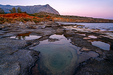 Aspes beach natural holes on the rocks full with water at sunset with turquoise water sea of Greece on the background