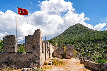 Turkish flag waiving in Kayakoy greek ghost town with abandoned houses in the mountains full of vegetations in Fethiye, Turkey