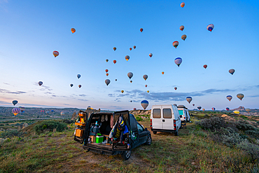 Camper vans parked in Love valley in front of hot air balloons at sunrise in Cappadocia, Turkey