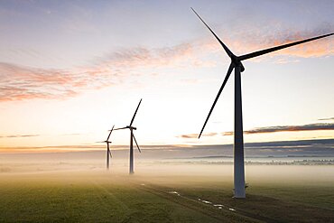 Aerial view of three wind turbines in the early morning fog at sunrise in the English countryside