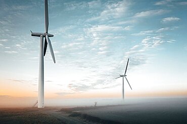 Aerial view of two wind turbines close up at sunrise in the fog in the English countryside