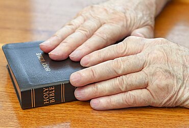 Old man hands on bible over table.