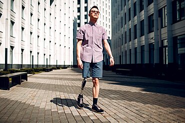 Disabled young man with foot prosthesis walks along the street.