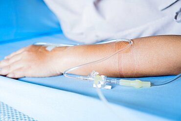 Patients saline, Iv drip, young woman hand with medical drip intravenous needle, give salt water on hospital bed. Intravenous therapy (IV) is a therapy that delivers fluids directly into vein.