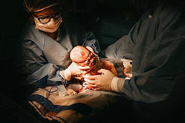 The medical team performing cesarean sections. The doctor holds the baby after birth to his mother to see. This image was taken at AIIMS hospital, New Delhi, on March 2015.