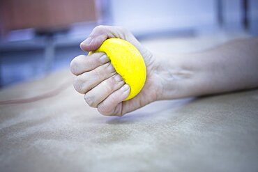 Female patient with physical injury and Rheumatoid arthritis squeezing physiotherapy ball with hand in hospital clinic resting on bed.