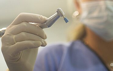 Dental instrumentation. Dental cleaning tool in the hand of dentist wearing a face mask in the dentists surgery clinic. Artistic color photo with shallow depth of focus.