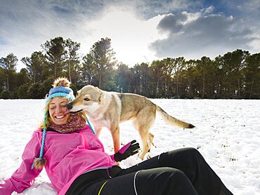 Caucasian young woman with hat and raincoat and wolf dog enjoying snow outdoor in winter time. Navarre, Spain, Europe.