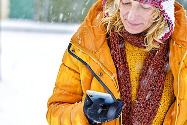 Caucasian young woman enjoying with a mobile phone in snow outdoor in winter time. Navarre, Spain, Europe.