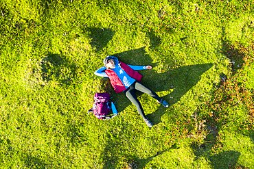 Aerial view of a young woman hiker lying on his back on a meadow. Aralar mountain range. Navarre, Spain, Europe.