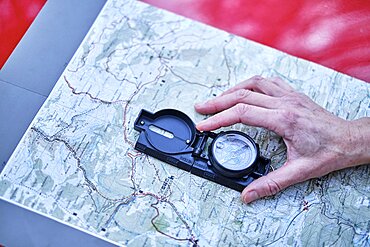 Young adult caucasian woman orienting herself with a map and a compass close to a car parked in a forestry path. Travels concept. Ayegui, Navarre, Spain, Europe.