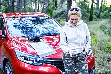 Young adult caucasian woman orienting herself with a map and a compass close to a car parked in a forestry path. Travels concept. Ayegui, Navarre, Spain, Europe.