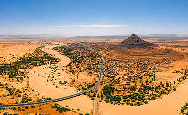 A crumbling mountain, a river bed, palms, and dunes surround the village of Kamour, Mauritania, Sahara Desert, West Africa, Africa