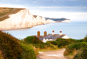 Coastguard cottages at Cuckmere Haven, with the white cliffs of Seven Sisters and Beachy Head in the background, Seaford, East Sussex, England