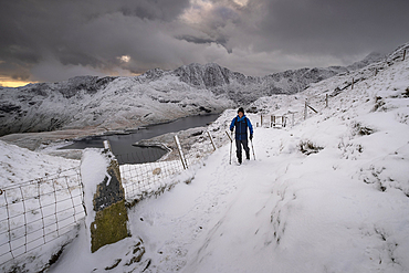 Walker on the PYG track backed by Cwm Dyli, Llyn Llydaw and Y Lliwedd in winter, Snowdonia National Park, Eryri, North Wales, United Kingdom, Europe