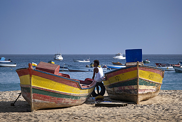 Local Man resting between colourful Fishing Boats on Praia de Santa Maria Beach, Santa Maria, Sal, Cape Verde Islands, Atlantic, Africa