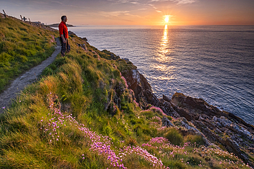 Walker looking out to sea from the Anglesey Coast Path at sunset in spring, near Cemaes, Anglesey, North Wales, UK