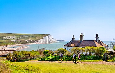 Walkers pass the Coastguard Cottages at Cuckmere Haven, East Sussex with the beach and the Seven Sisters behind.