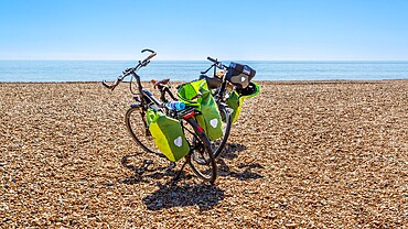 Touring bicycles parked on a sunny pebble beach in East Sussex, England, UK.
