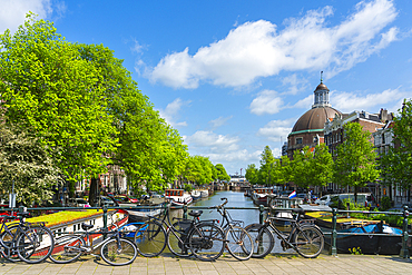 Bikes on Corsgenbrug bridge over Singel canal and Renaissance dome of Koepelkerk Church in the background, Amsterdam, The Netherlands, Europe