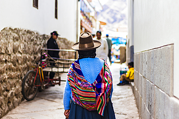 Woman walking away in narrow street with traditional colorful Peruvian bag over her back, Pisaq, Peru, South America