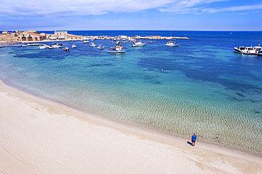 Aerial view of tourist standing in an empty white sand beach looking at the sea in front of the fishing village of Marzamemi, Marzamemi, Pachino municipality, Siracusa province, Sicily, Italy, Mediterranean, Europe