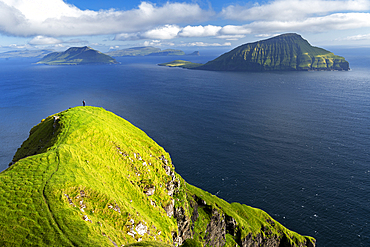 Hiker walks on top of a tall cliff overlooking the ocean, Nordradalur, Streymoy island, Faroe islands, Denmark, Europe