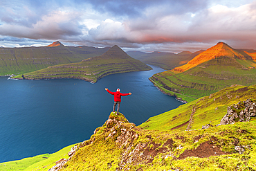 Happy hiker stands on top of the cliff overlooking the fjord of Funningur, Eysturoy island, Faroe islands, Denmark, Europe