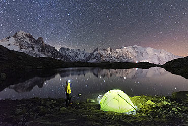 Person admiring the starry sky outside tent pitched on the shore of Cheserys lake surrounded by alpine landscape of Mont Blanc, Chamonix, Haute Savoie, French Alps, France, Europe