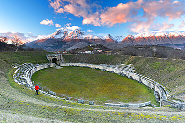 Man enjoys the view of the old amphitheatre and snowy peak at sunset, Alba Fucens, L'Aquila, Apennines, Abruzzo, Italy, Europe