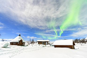 Typical wooden buildings covered with snow under the Northern Lights (Aurora Borealis), full moon night, Kilpisjarvi, Enontekio municipality, Finnish Lapland, Finland, Scandinavia, Europe