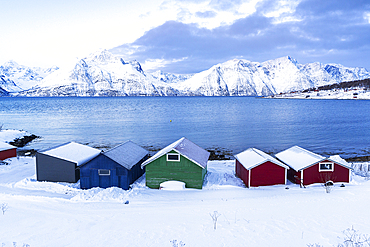 Colorful wooden rorbu covered with snow in the icy landscape by the fjord, Djupvik, Olderdalen, Lyngen fjord, Lyngen Alps, Troms og Finnmark, Norway, Scandinavia, Europe