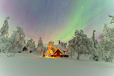 Hiker with lantern beside a mountain hut exlores the snowy forest under Northern Lights (Aurora Borealis), Pallas-Yllastunturi National Park, Muonio, Finnish Lapland, Finland, Scandinavia, Europe