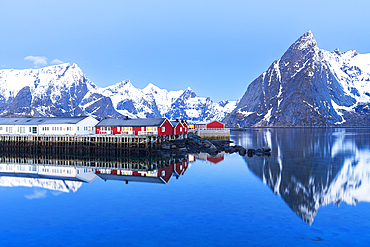 Dusk over the fishing village and the calm water of the fjord surrounded by snowy mountains, Hamnoy, Reine, Moskenes, Lofoten Islands, Norway, Scandinavia, Europe