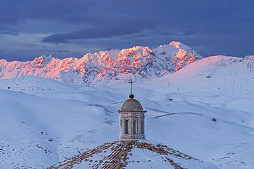 Close-up view of the roof of the church of Santa Maria della Pieta with snow covered mountains of Gran Sasso lit at sunset, Rocca Calascio, Gran Sasso e Monti della Laga National Park, Campo Imperatore, L'Aquila province, Abruzzo, Italy, Europe