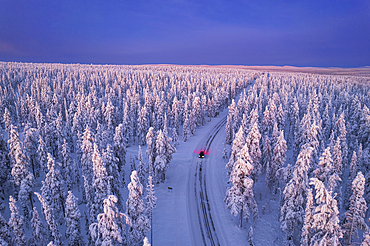 Aerial view of a car driving through the winter forest covered from snow at dawn, Akaslompolo, Kolari, Pallas-Yllastunturi National Park, Lapland region, Finland, Europe