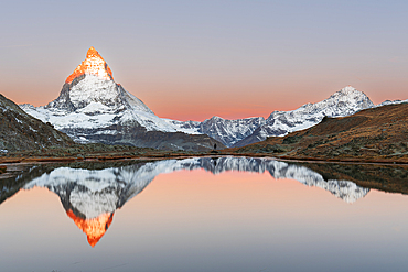 Hiker admiring the Matterhorn reflected in the Riffelsee lake at sunrise, Gornergrat, Zermatt, canton of Valais, Switzerland, Europe