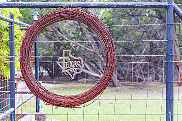 Boerne, Texas, USA. April 14, 2021. A spool of barbed wire and a Texas sign on a fence.