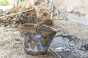 Mavzoley Rudaki, Sughd Province, Tajikistan. A muddy bucket being used to apply mud plaster to a traditional stone house.