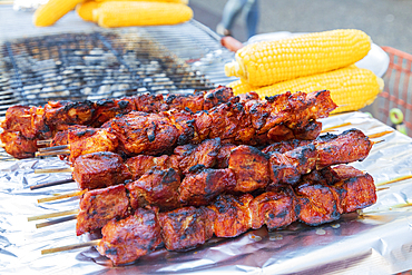 Jackson Heights, Queens, New York City, New York, USA. Meat kebabs and corn on the cob at a sidewalk food stand.