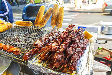 Jackson Heights, Queens, New York City, New York, USA. Meat kebabs and corn on the cob at a sidewalk food stand.