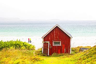 Two people walking on Ramberg beach on an autumn day, with a famous cabin in foreground, Lofoten Islands, Nordland, Norway, Scandinavia, Europe