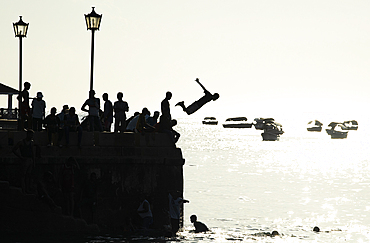 Silhouetted teenagers dive into the sea from the town pier, Stone Town, Zanzibar island, Tanzania, East Africa, Africa