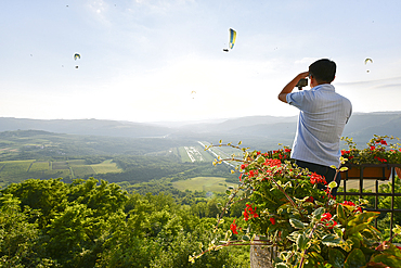 A tourist photographs paragliders from atop the hilltop village of Motovun, Istria, Croatia, Europe