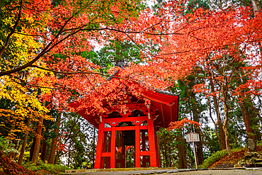 Iconic red Shōrō bell tower framed by vivid autumn leaves on Mount Hiei, near the historic Enryaku-ji Temple in Japan.